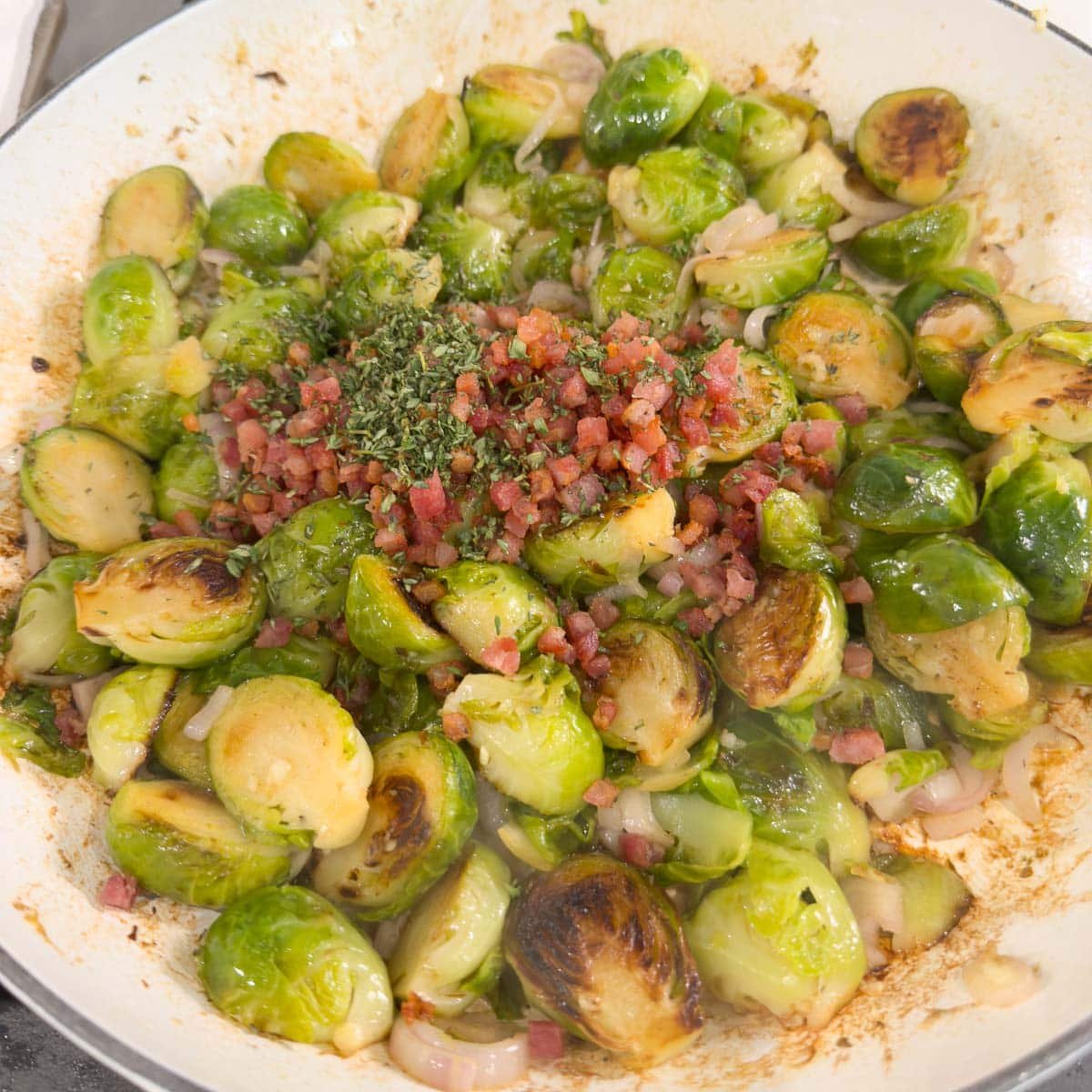 Cooked Brussels sprouts with pancetta and herbs in a pan.