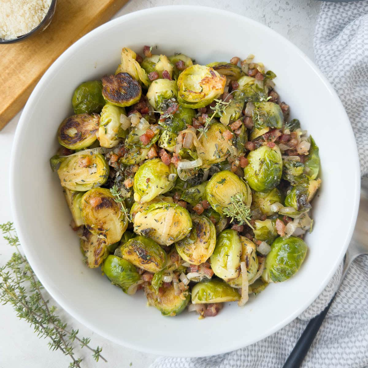 Rund bowl of golden green Brussels sprouts with pancetta, herbs, and shallots ready for serving.