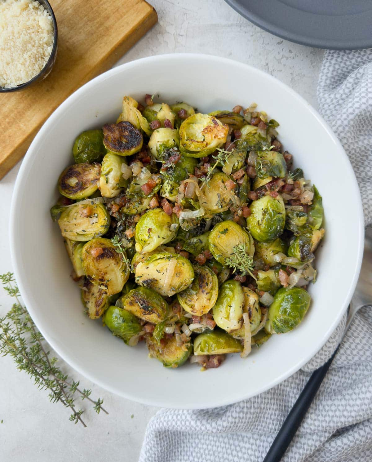 White bowl of tender Brussels sprout with crisp pancetta, herbs, and shallots. 
