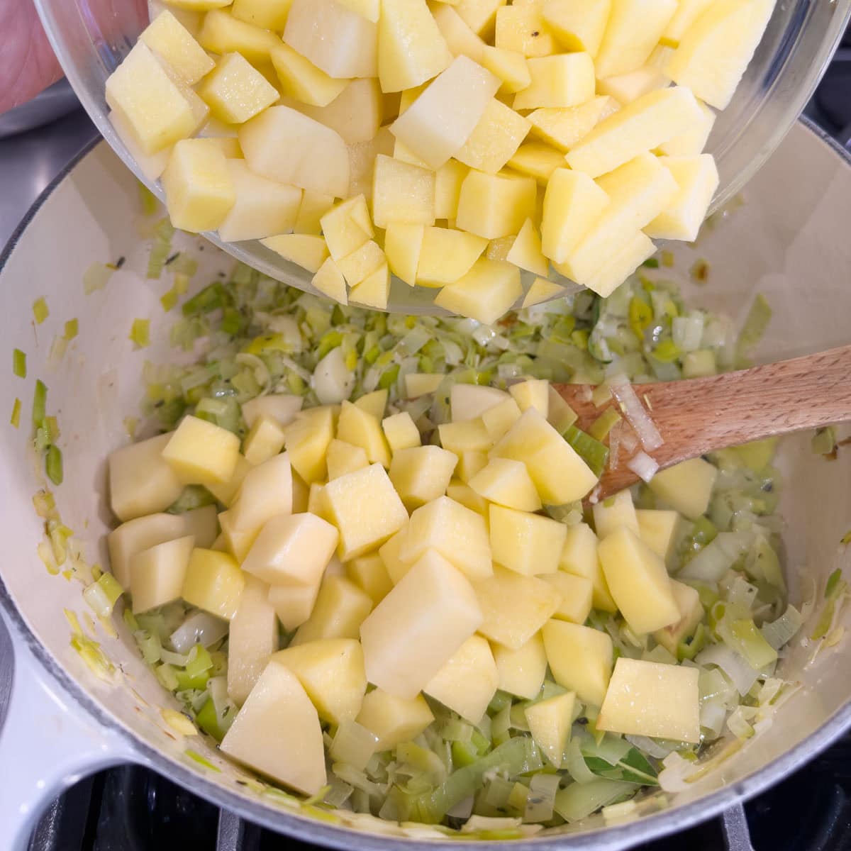 Adding chopped gold potatoes to a pot of simmering broth and vegetables for soup.