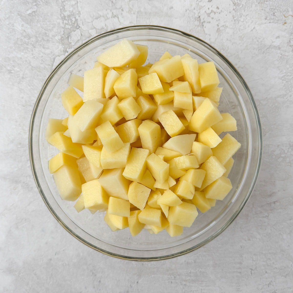 A glass bowl of chopped gold potatoes for leek and potato soup.