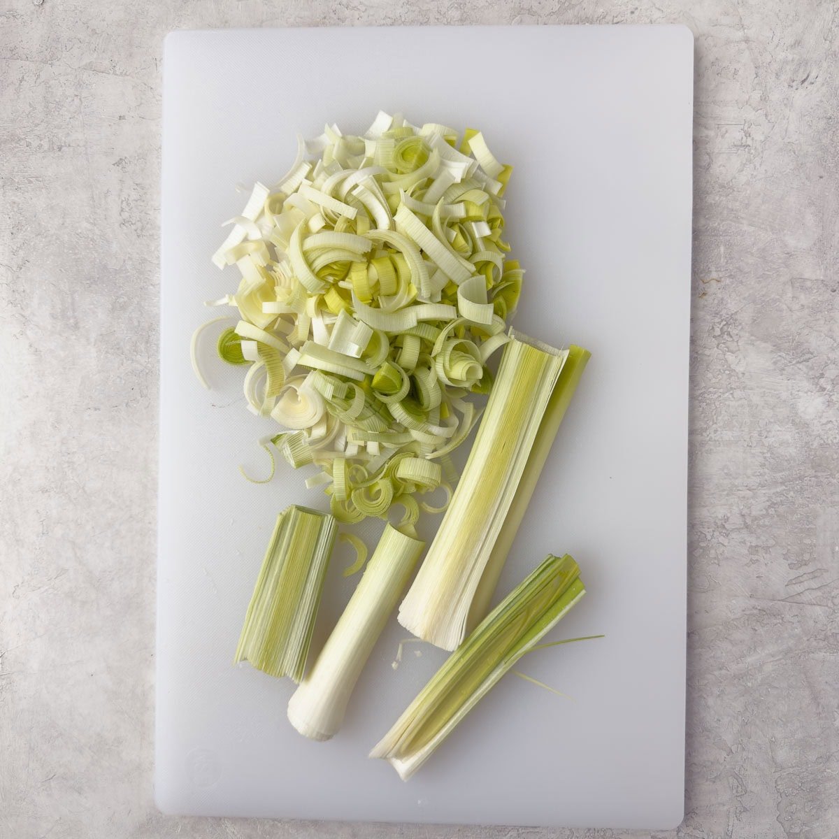 Prep work of split leeks, then chopping crosswise into pieces on a white cutting board.