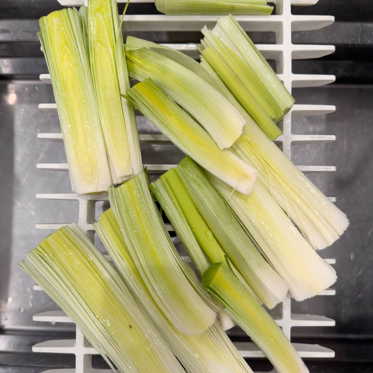 Rinsing split leeks under cold water in a sink.