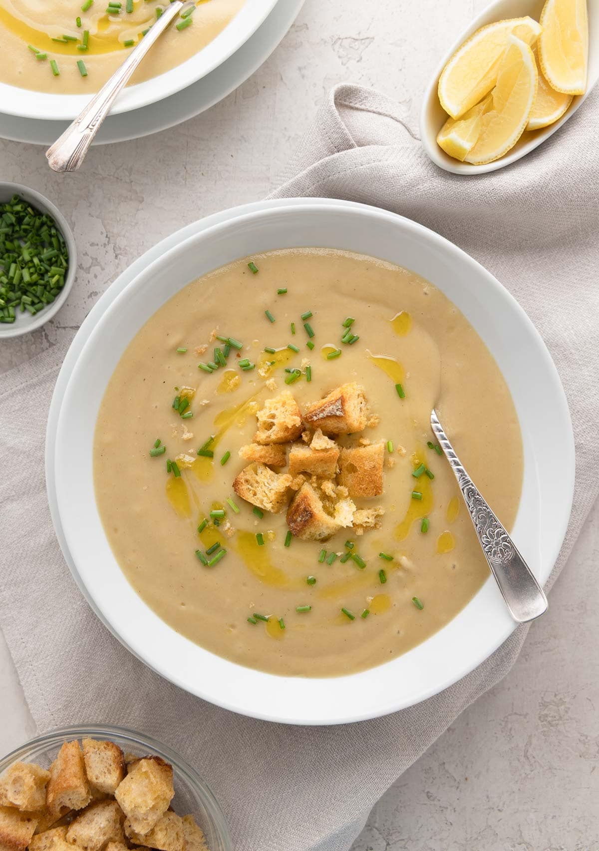 Bowls of pale golden creamy leek and potato soup with croutons and chives.