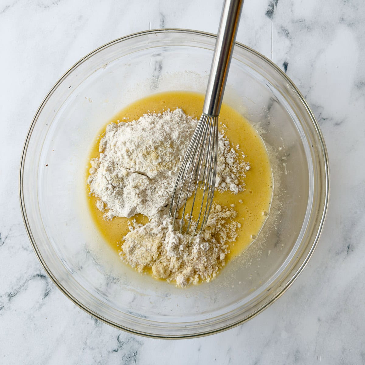 Mixing batter for a Nantucket cranberry pie in a glass bowl with silver whisk.