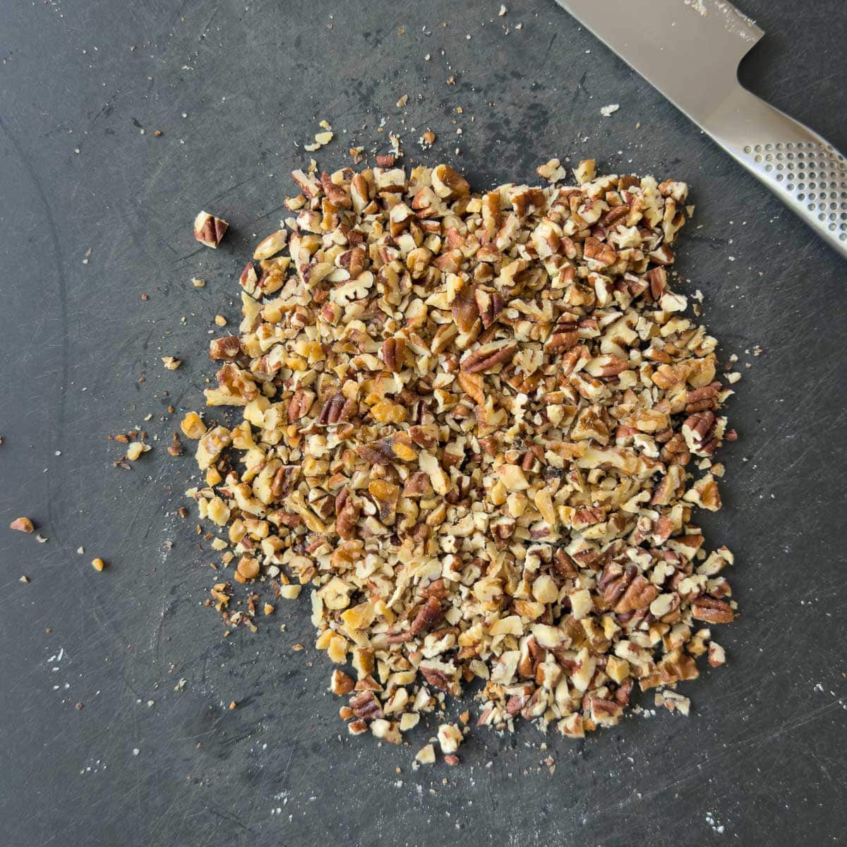 Chopped nuts on a black cutting boards with a chef's knife.