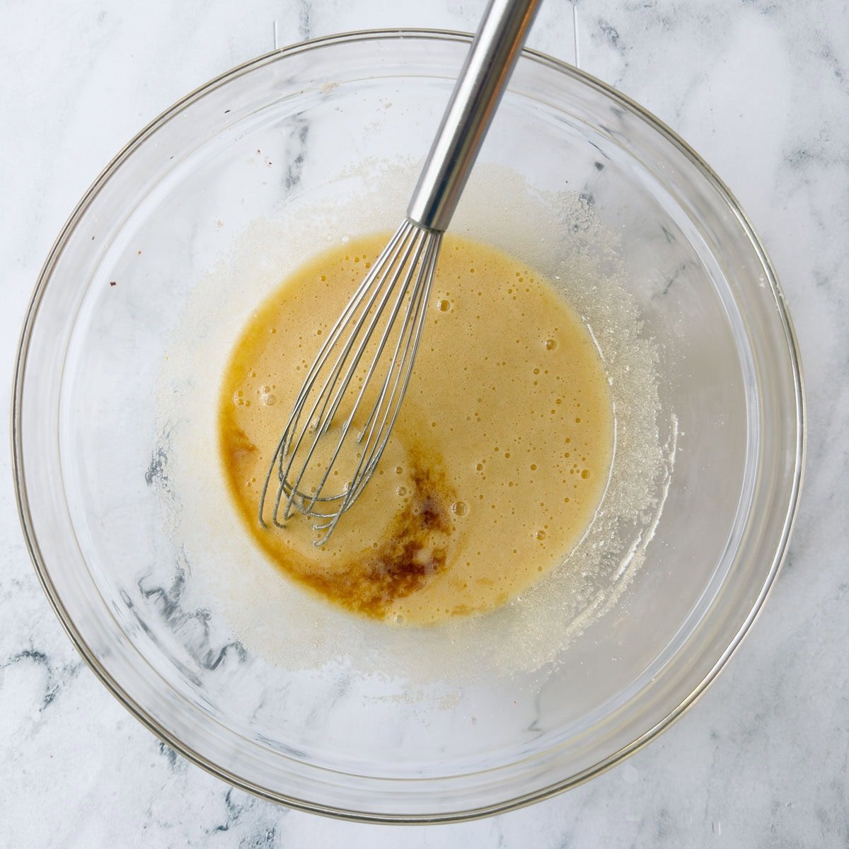 Whisking eggs and sugar in a glass bowl with vanilla extract.