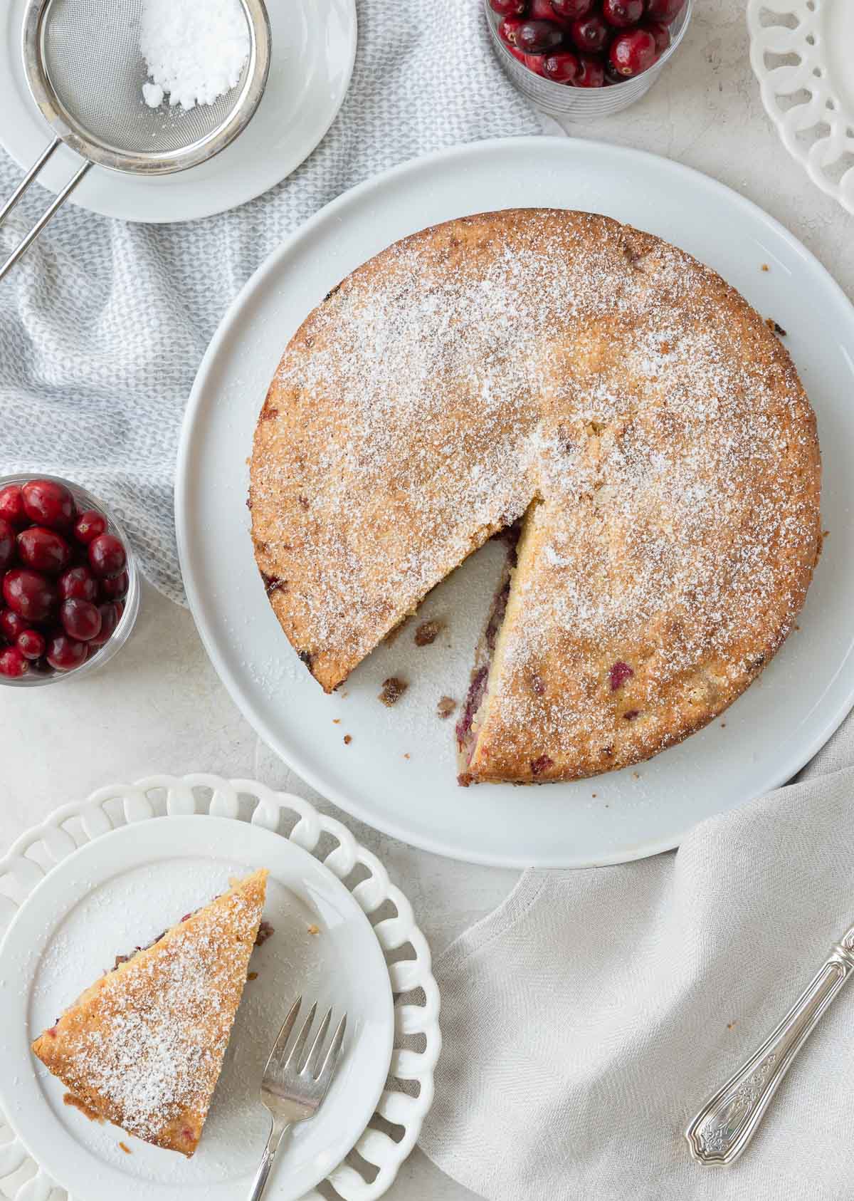 A nantucket cranberry pie on a plate, with a slice out, cranberries beside 
