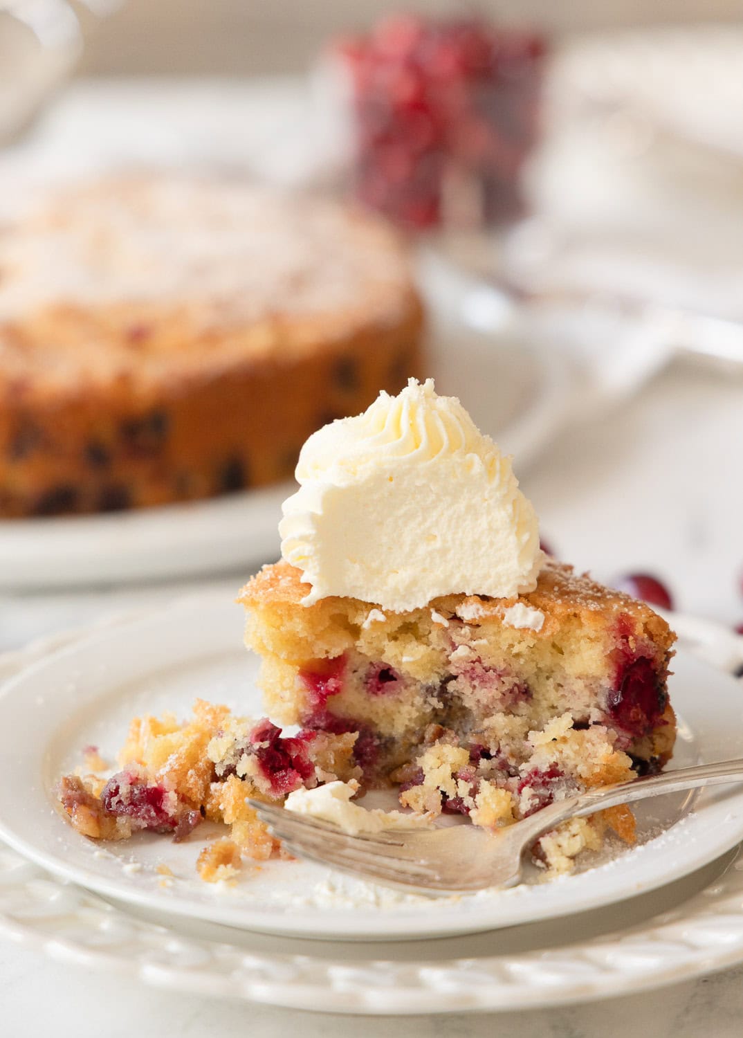 A slice of cranberry nantucket pie with stiff whipped cream on top, with a silver fork on a plate.