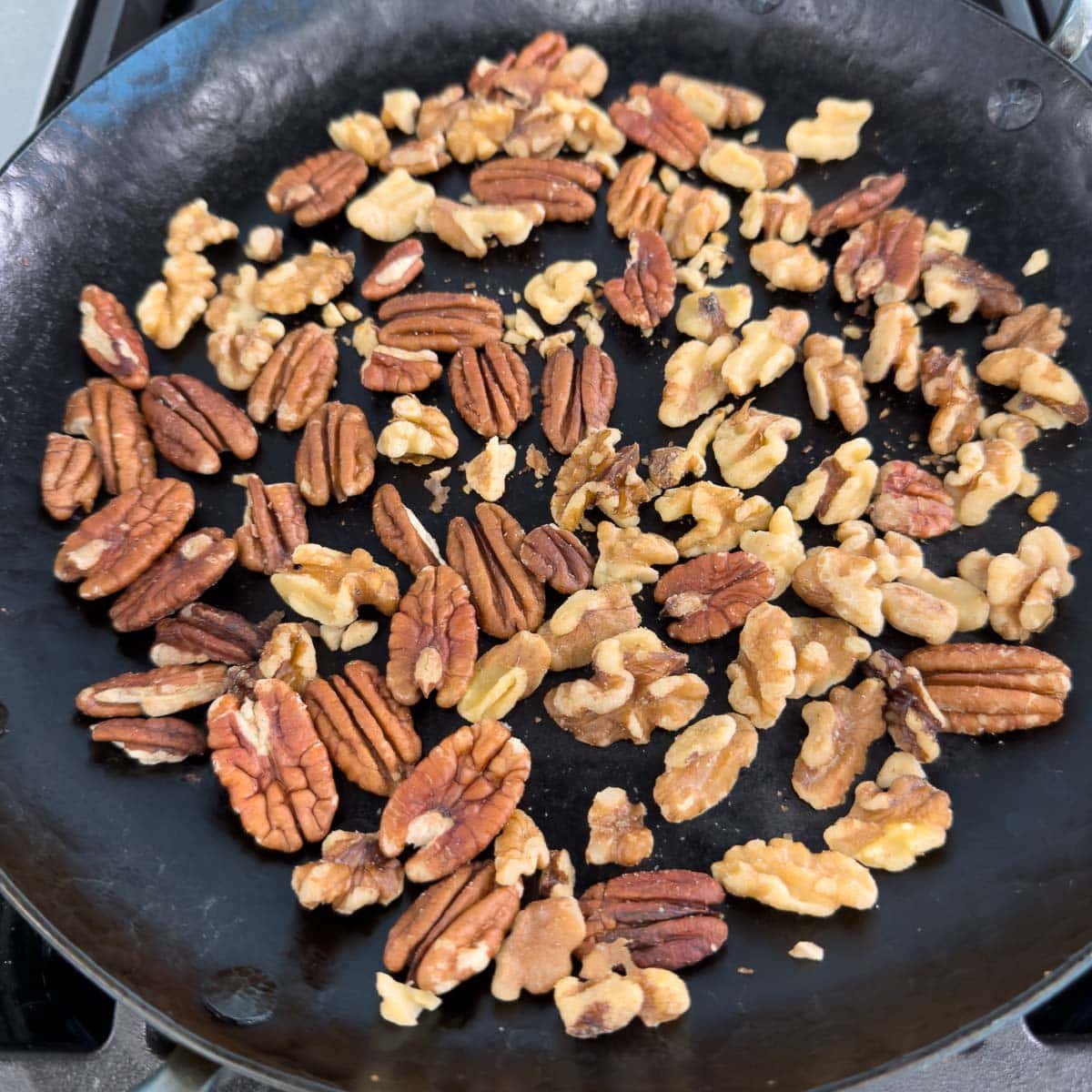 Toasting walnuts and pecans in a black iron skillet.