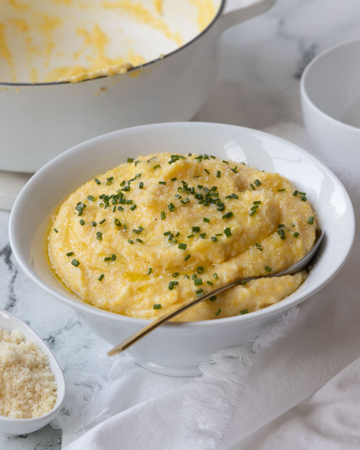 White bowl of golden creamy polenta with chopped chives and olive oil drizzle. 
