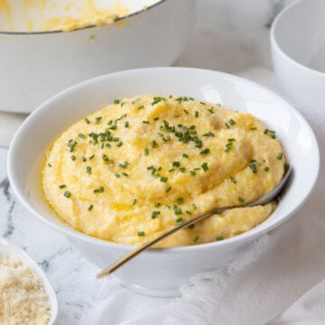A bowl of rich yellow polenta with chives and a serving spoon.