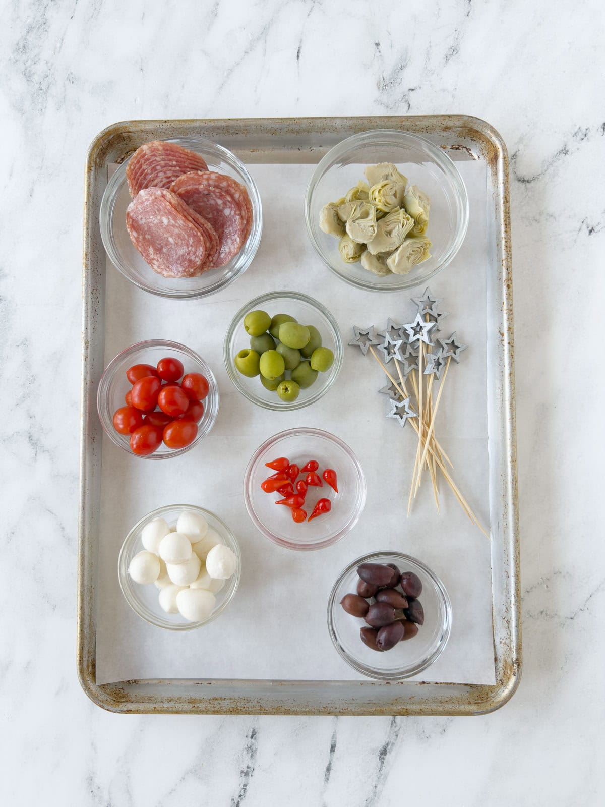A tray set up to assemble antipasto skewers with fancy picks and all ingredients.