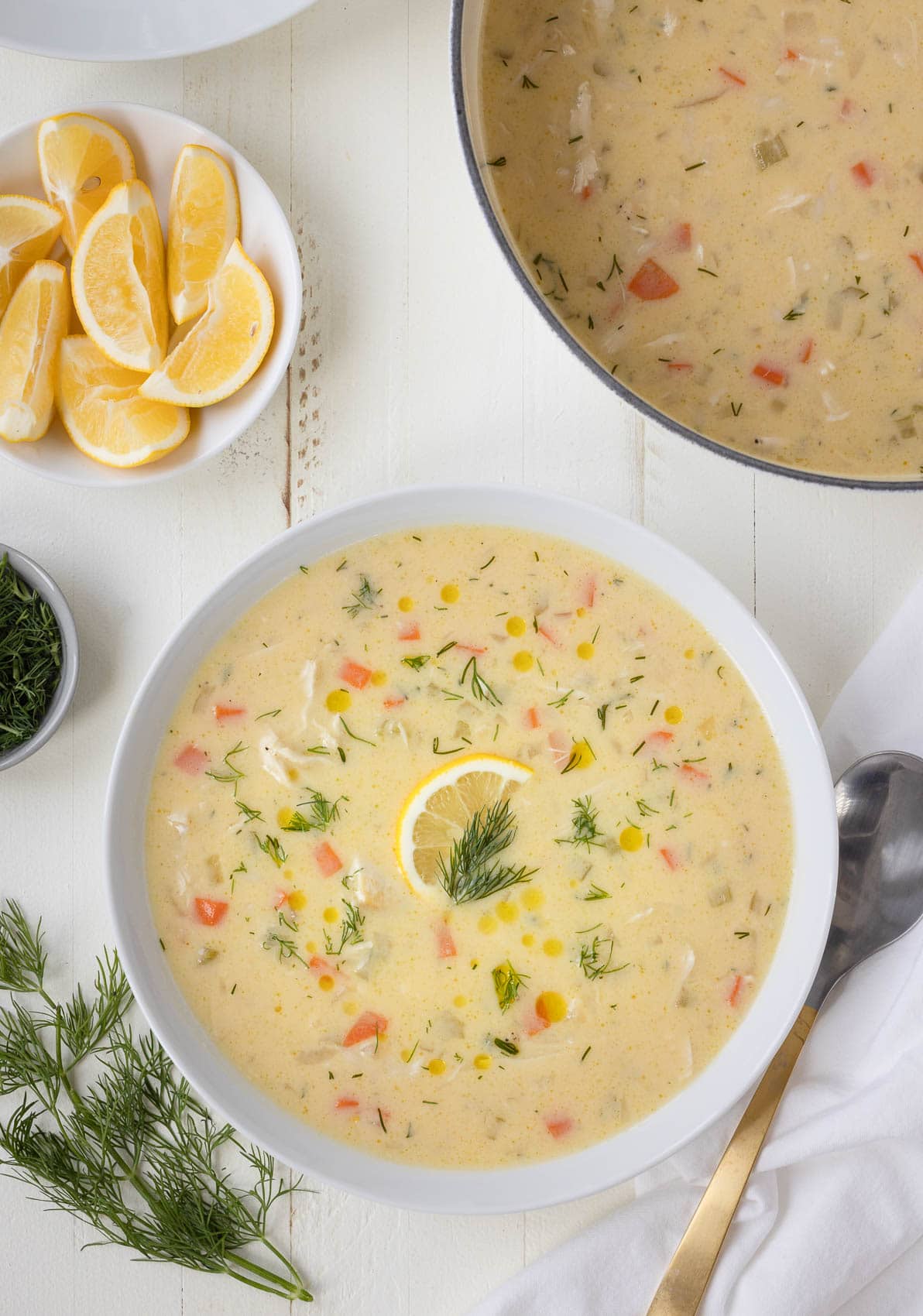 Greek lemon chicken soup, called avgolemono, in a white bowl with lemon slice and fresh dill.