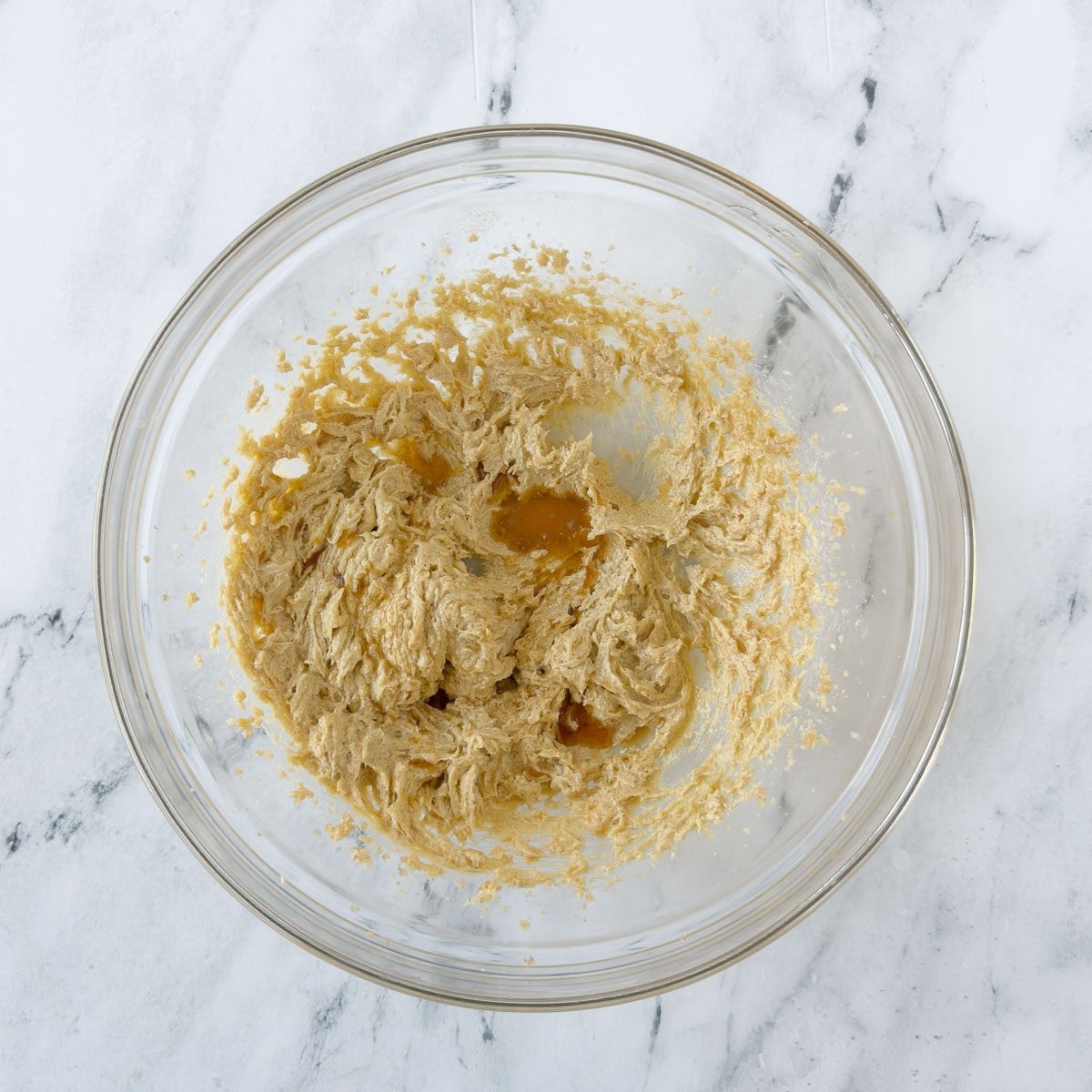 Creaming butter and sugar, adding vanilla, for cookie dough in a glass bowl.