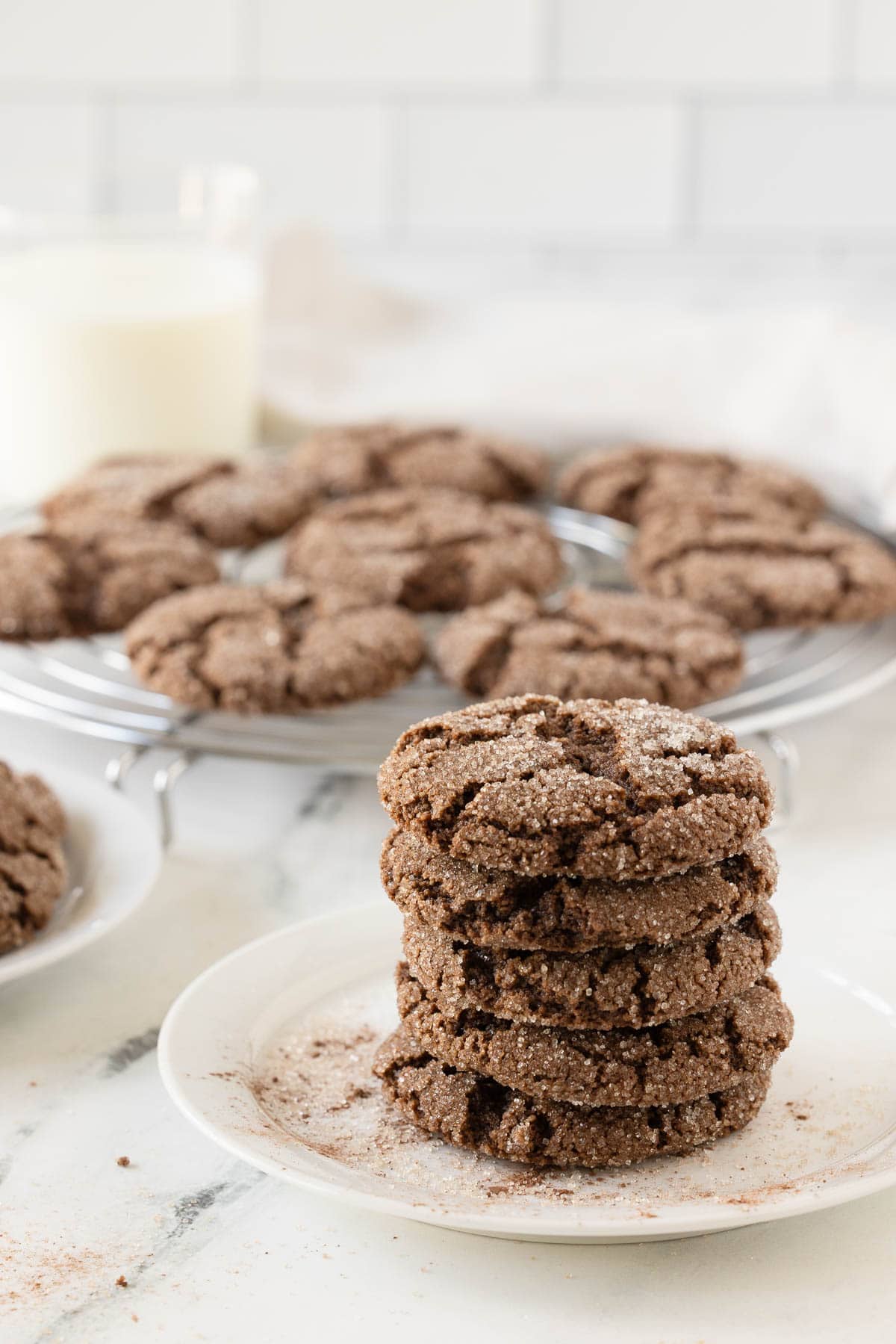 A stack of chocolate almond cookies on a white plate with cooling cookies behind.