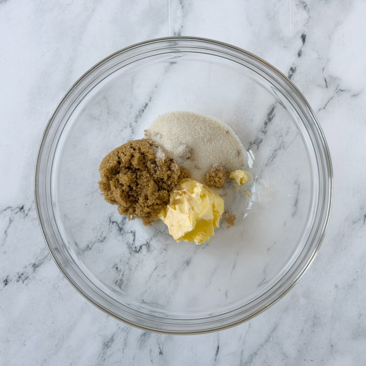 Brown sugar, sugar, and butter in a glass bowl for creaming into a cookie dough.