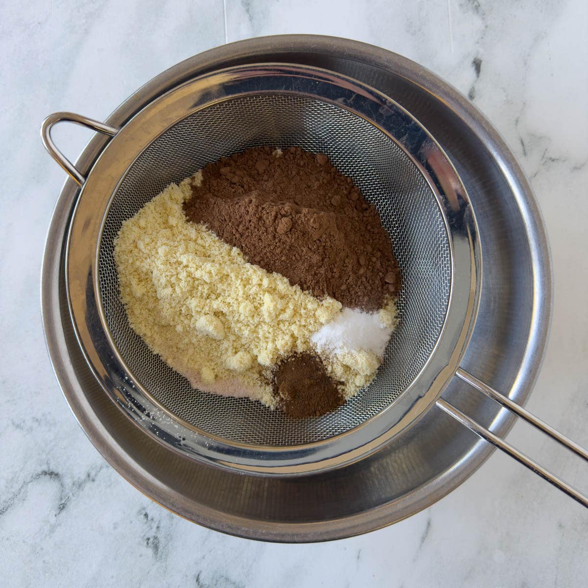 Cocoa powder, almond flour, and baking soda in a fine sieve for sifting into a bowl.