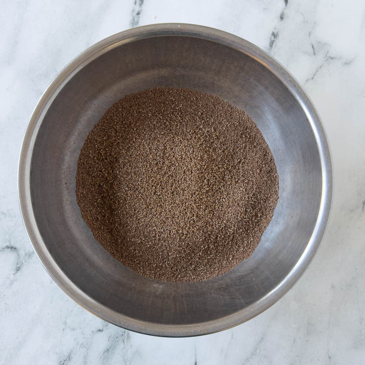 Sifted cocoa powder, flour, and dry ingredients for chocolate almond flour cookies in a stainless bowl.