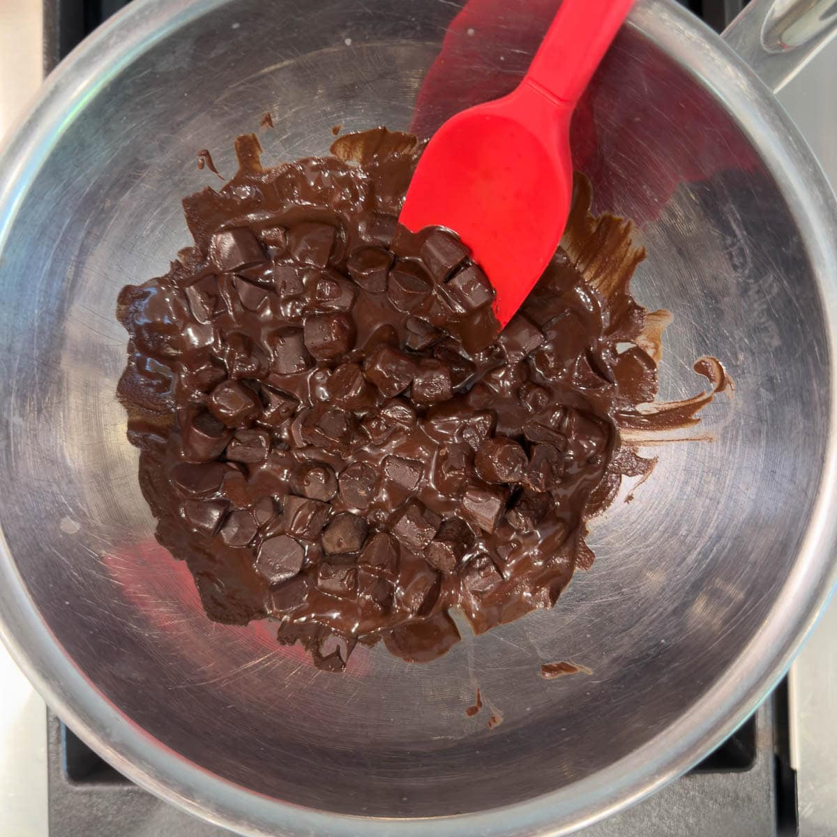 melting dark chocolate in a stainless steel bowl with a red spatula.