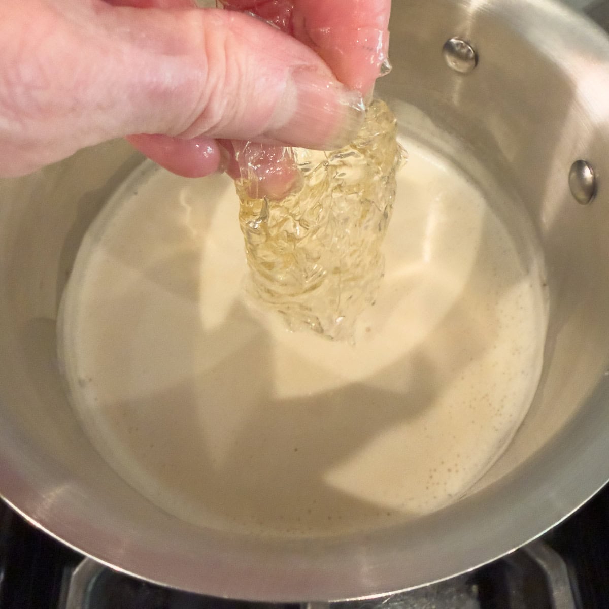 Adding softened gelatin to warm cream in a pot.
