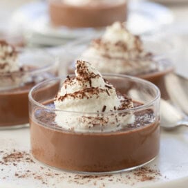 Glass cup of dark chocolate panna cotta with whipped cream and chocolate shavings.