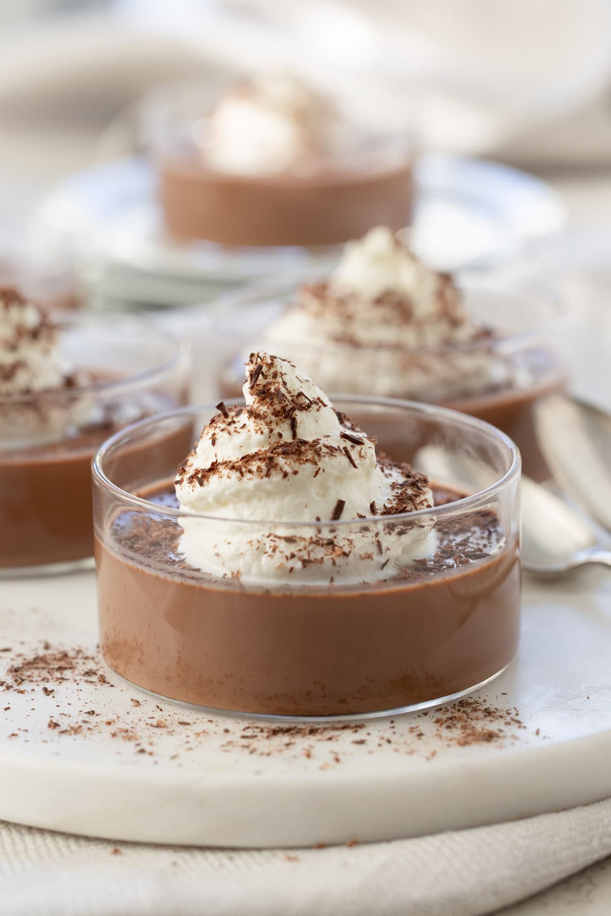 A glass ramekin of chocolate panna cotta with whipped cream and chocolate shavings.