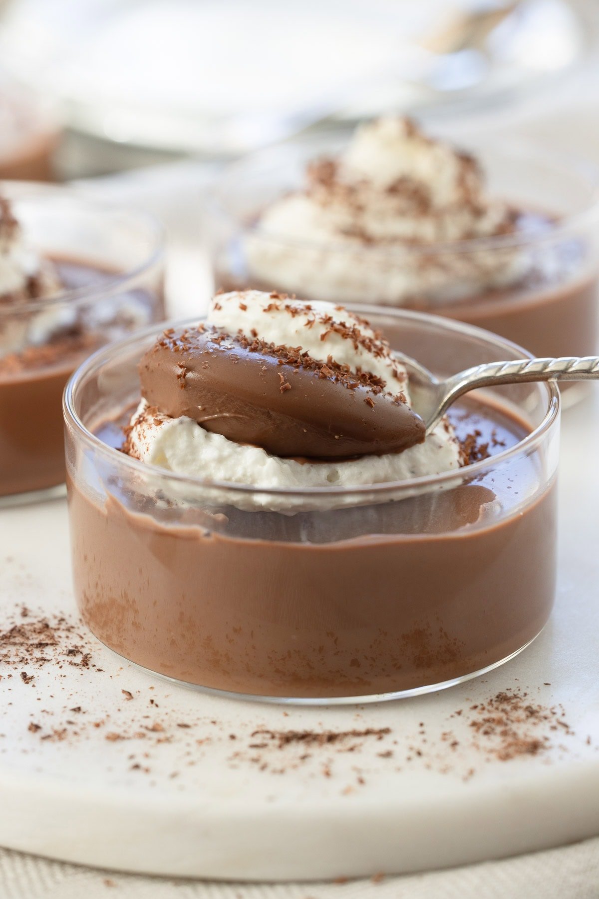 A spoonful of silky chocolate panna cotta with whipped cream on a silver spoon with chocolate sprinkles.