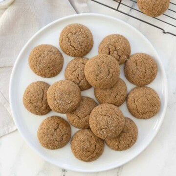 A plate of golden sugar sprinkled ginger cookies with more cooling on a wire rack.
