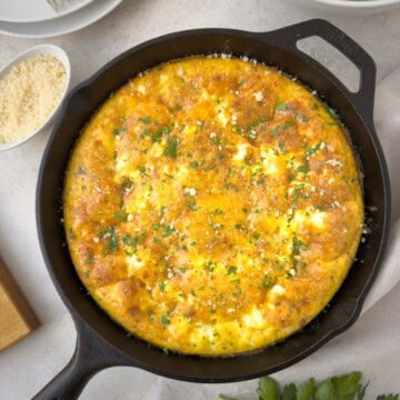 A golden cheesy frittata in a cast iron skillet sprinkled with parmesan and chopped parsley.