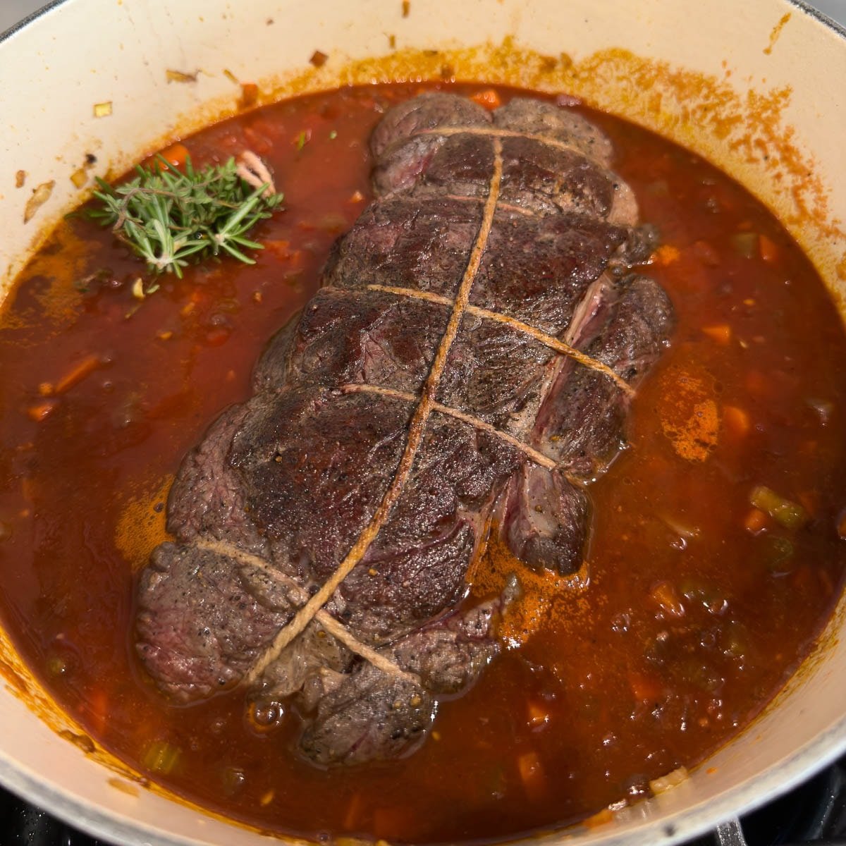 Pot roast added to a pot of broth, reduce wine and vegetables for cooking.