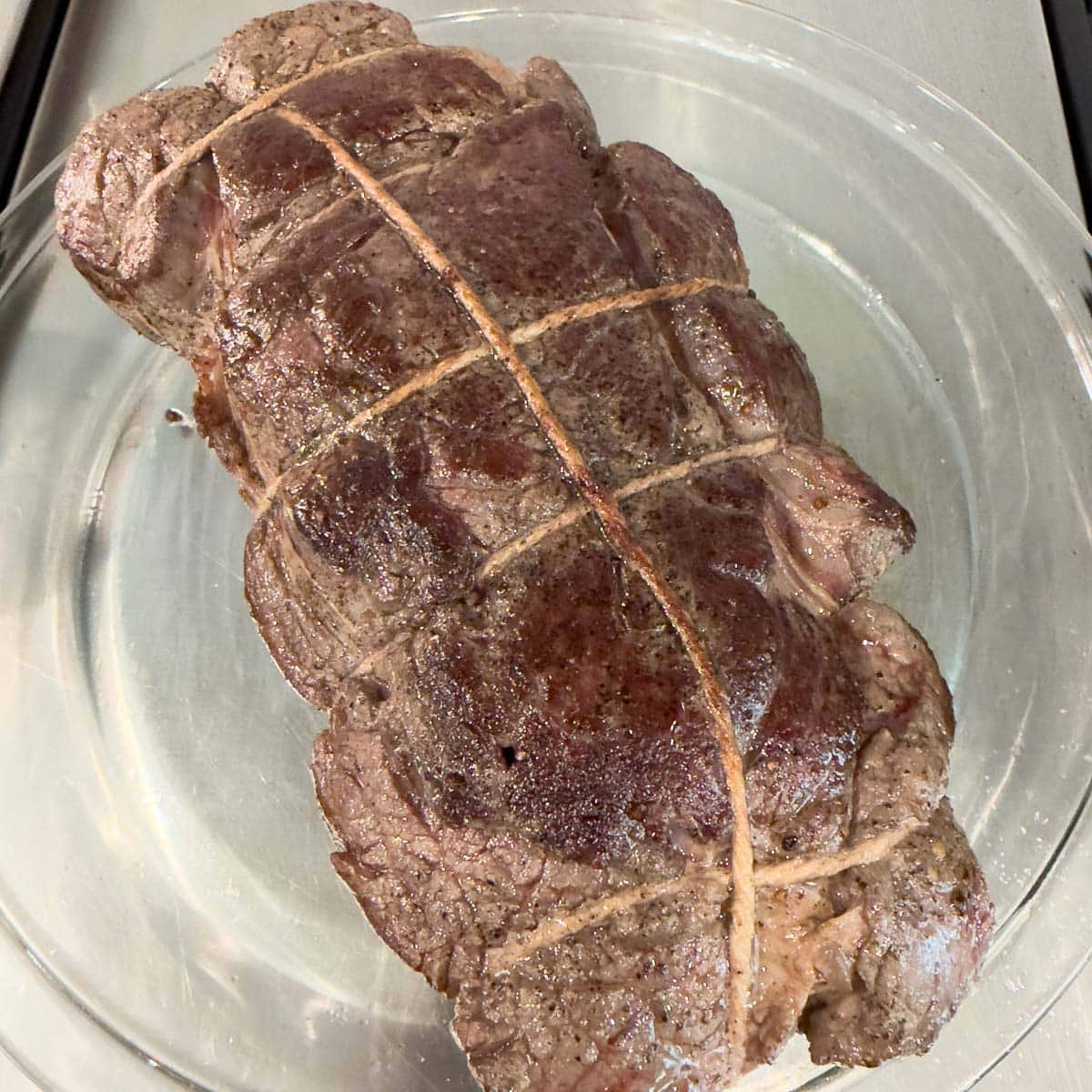 A nicely browned roast of beef on a plate waiting for next steps in the process.