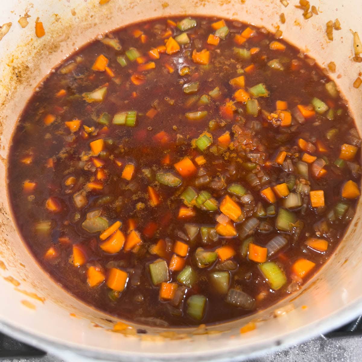 Red wine reducing in a large pot with vegetables to create a braising base. 