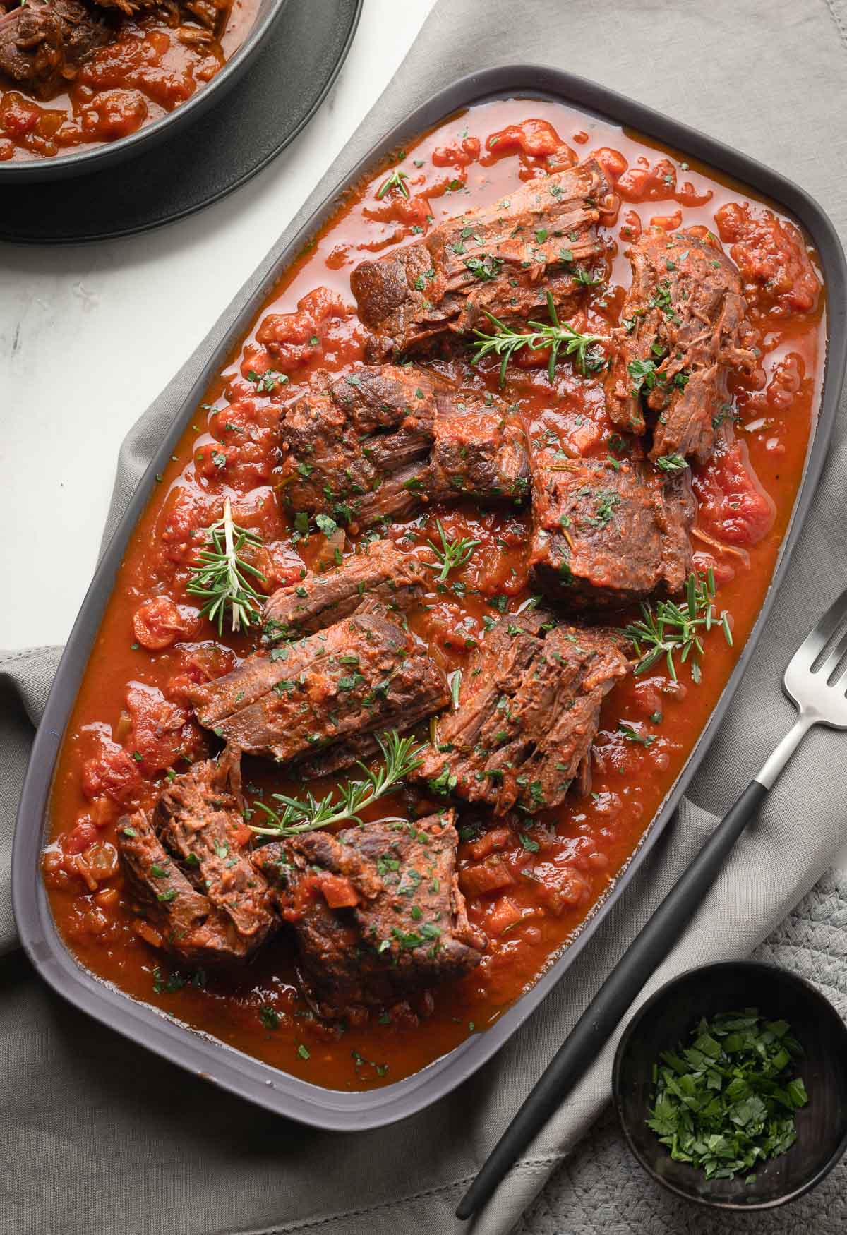 Italian pot roast, called stracotto, with chunks of meat and red sauce on a gray platter. 