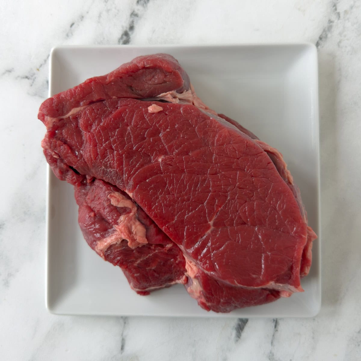 a raw red chuck roast on a plate on the counter.