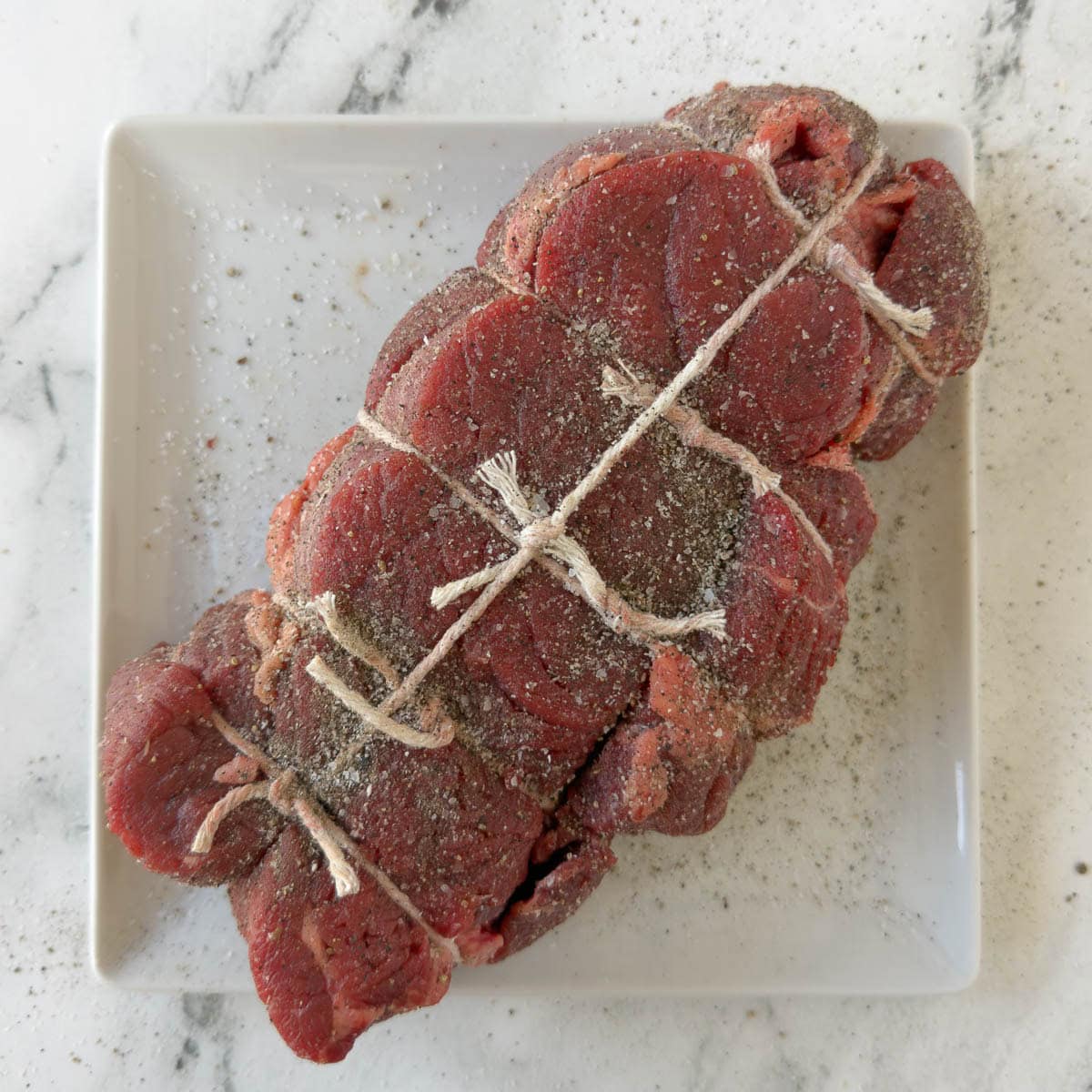 A tied raw chuck roast ready for seasoning and cooking.