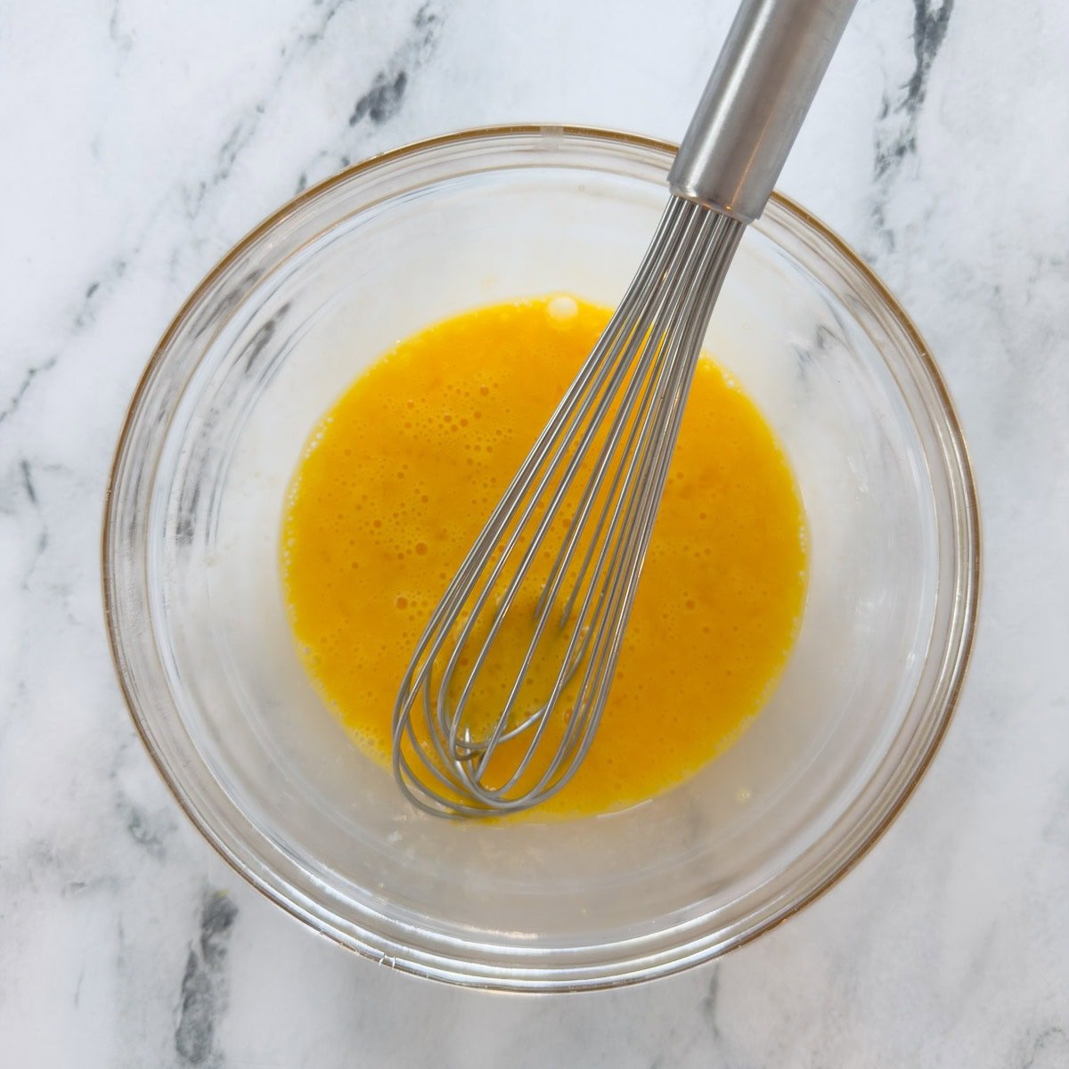 Whisking eggs and lemon juice together in a glass bowl.
