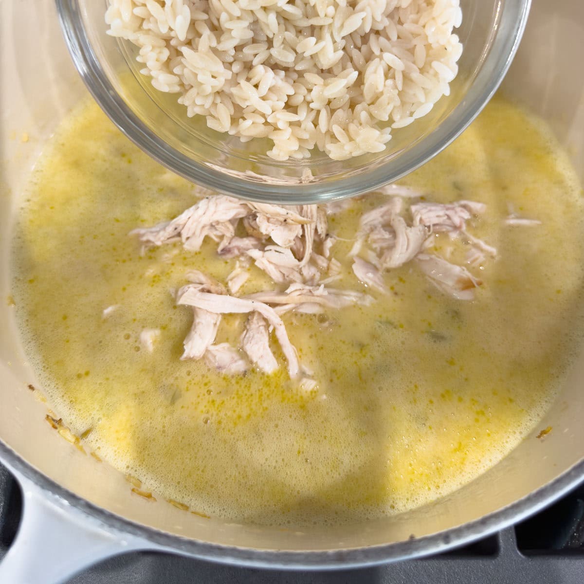 Shredded chicken breast being added to avgolemono lemon chicken soup.