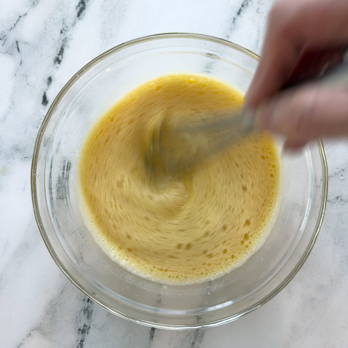 Tempering eggs, broth and lemon juice together with a silver whisk.