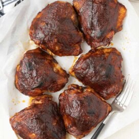 Plate of burnished glossy barbecue chicken thighs with serving fork.