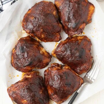 Plate of burnished glossy barbecue chicken thighs with serving fork.