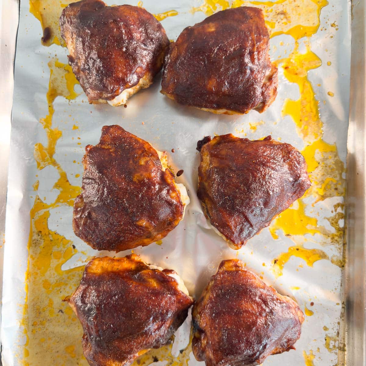 Six glossy baked bbq chicken thighs on a baking sheet, ready to serve.