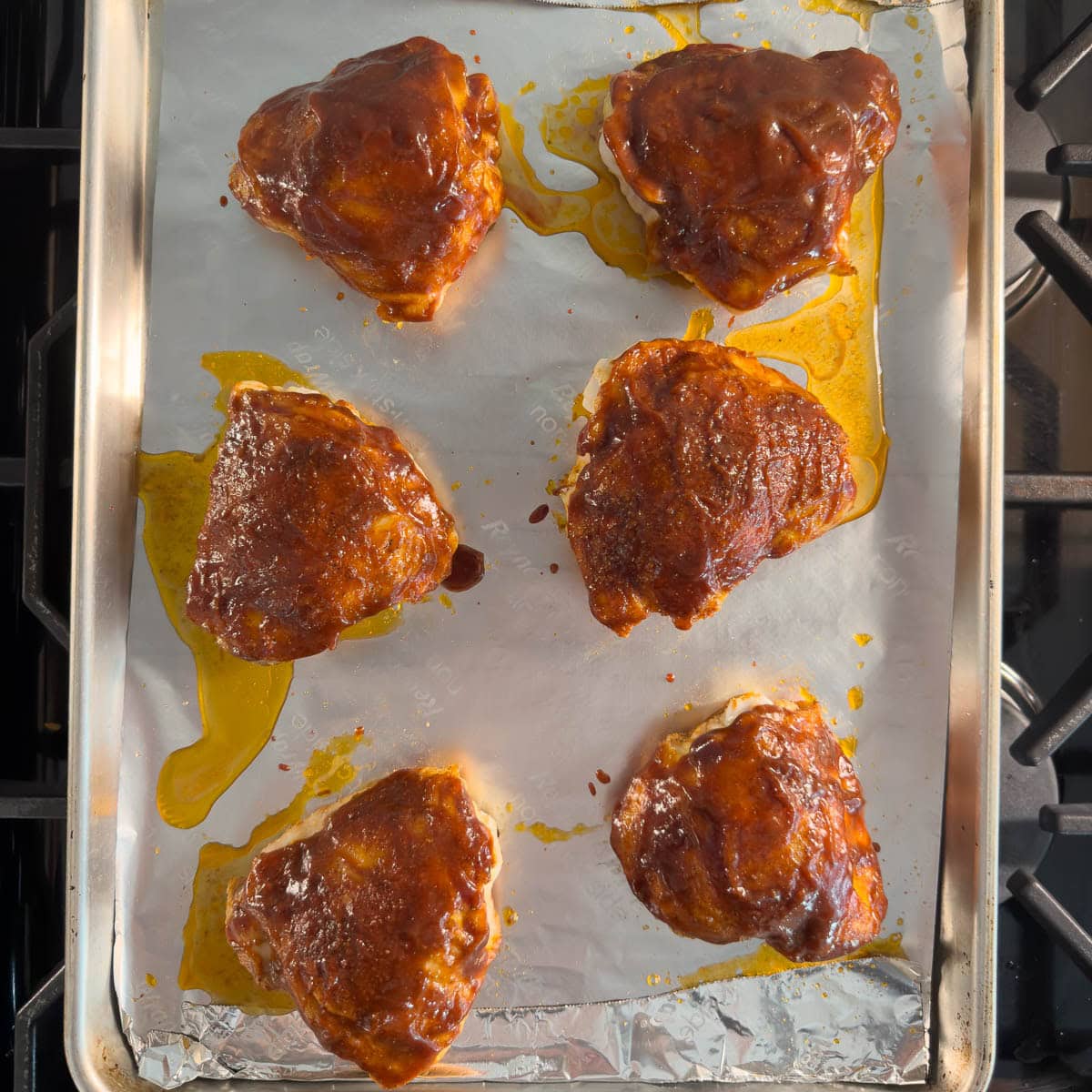 Partially baked chicken thighs on a baking sheet with bbq glaze.