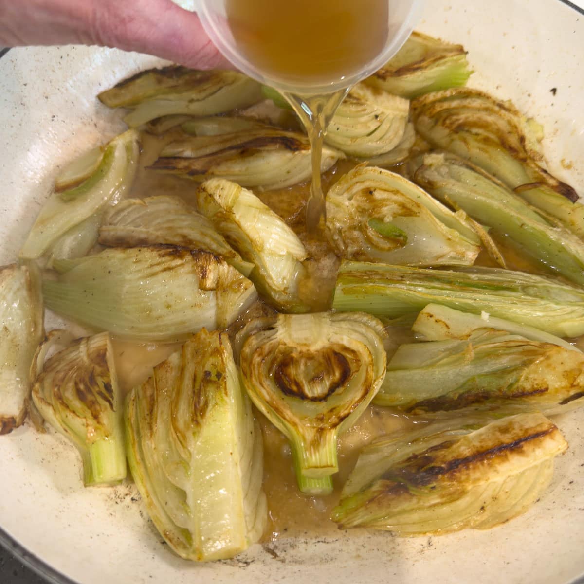 Pouring chicken broth into a pan for braising.