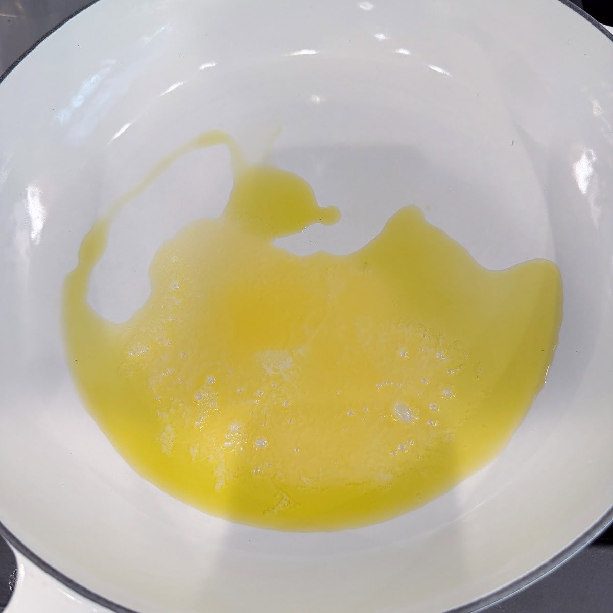 Melted butter in a white wide round braiser pan.