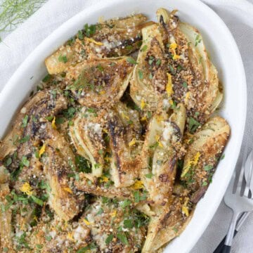 An oval baking dish with braised fennel and a crunchy topping or parmesan and toasted breadcrumbs.