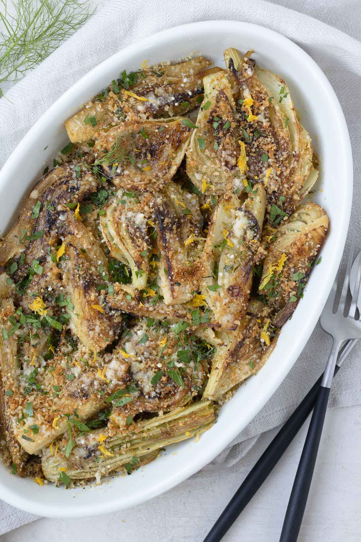 Oval casserole dish with golden braised fennel topped with parmesan cheese, toasted breadcrumbs, and herbs.