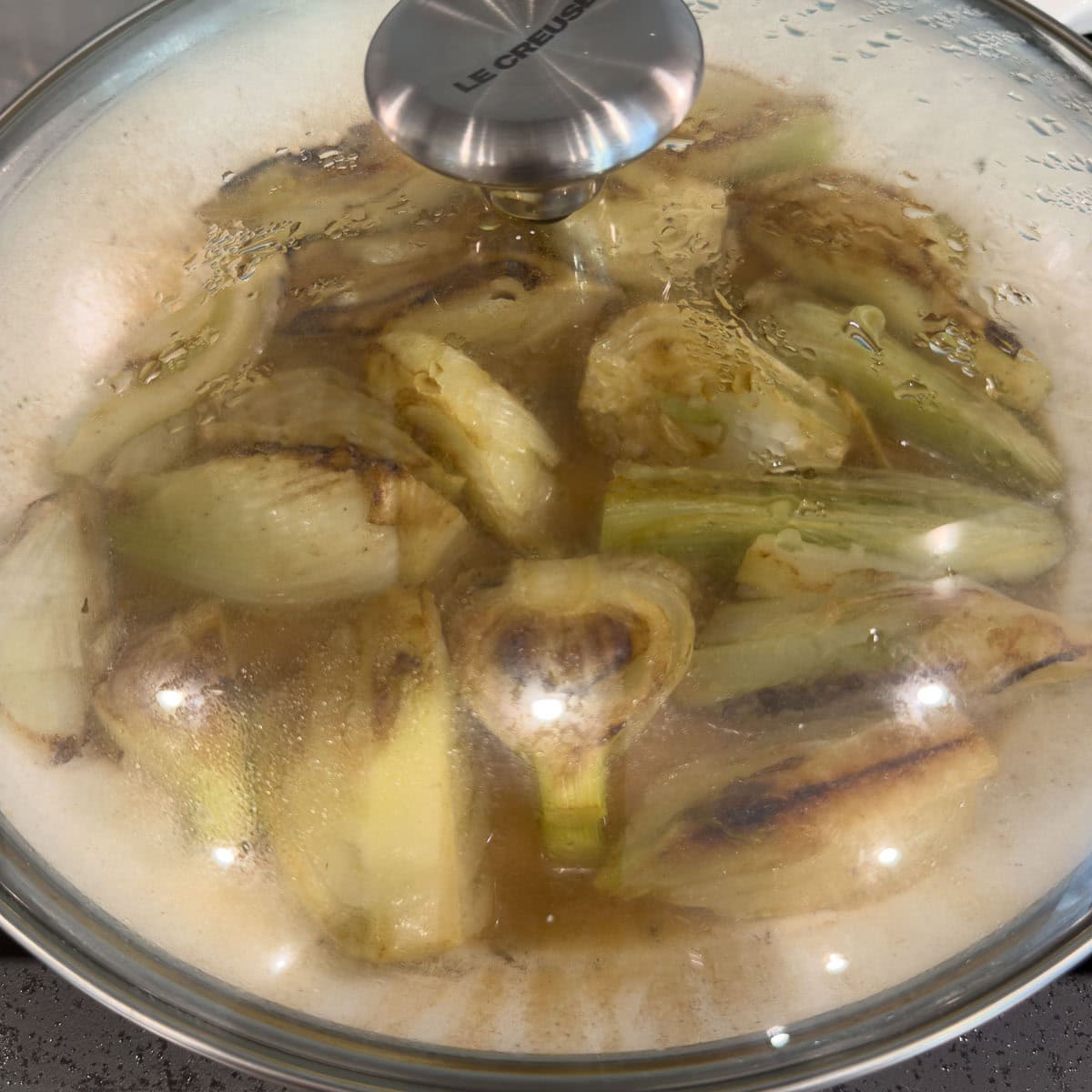 A glass lid on a pan showing fennel cooking inside.