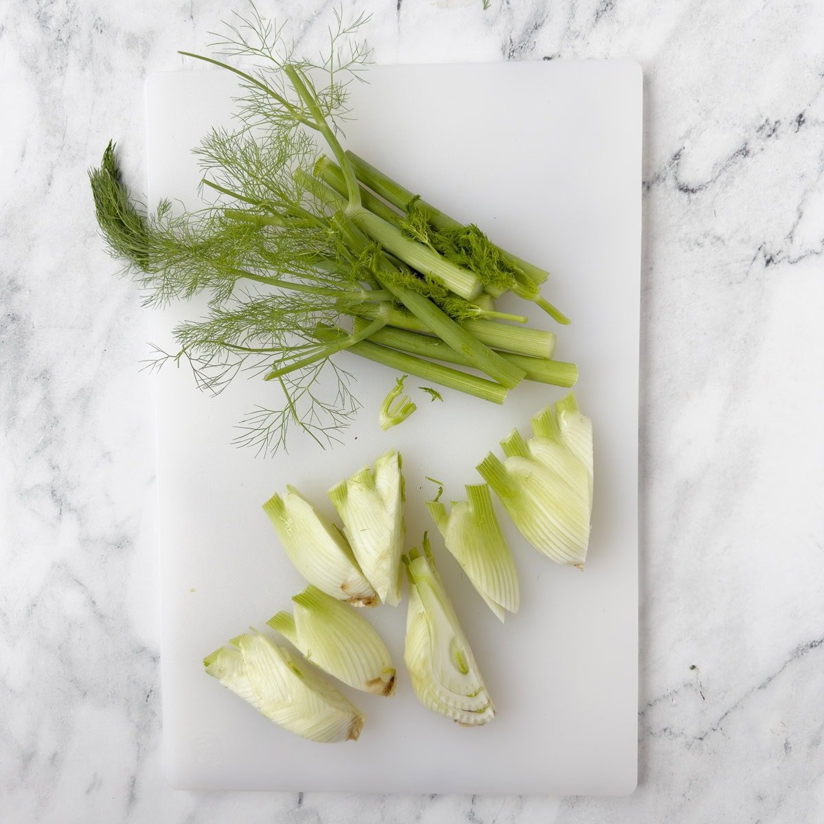 Prepping fennel for cooking by trimming stalks and cutting into wedges.