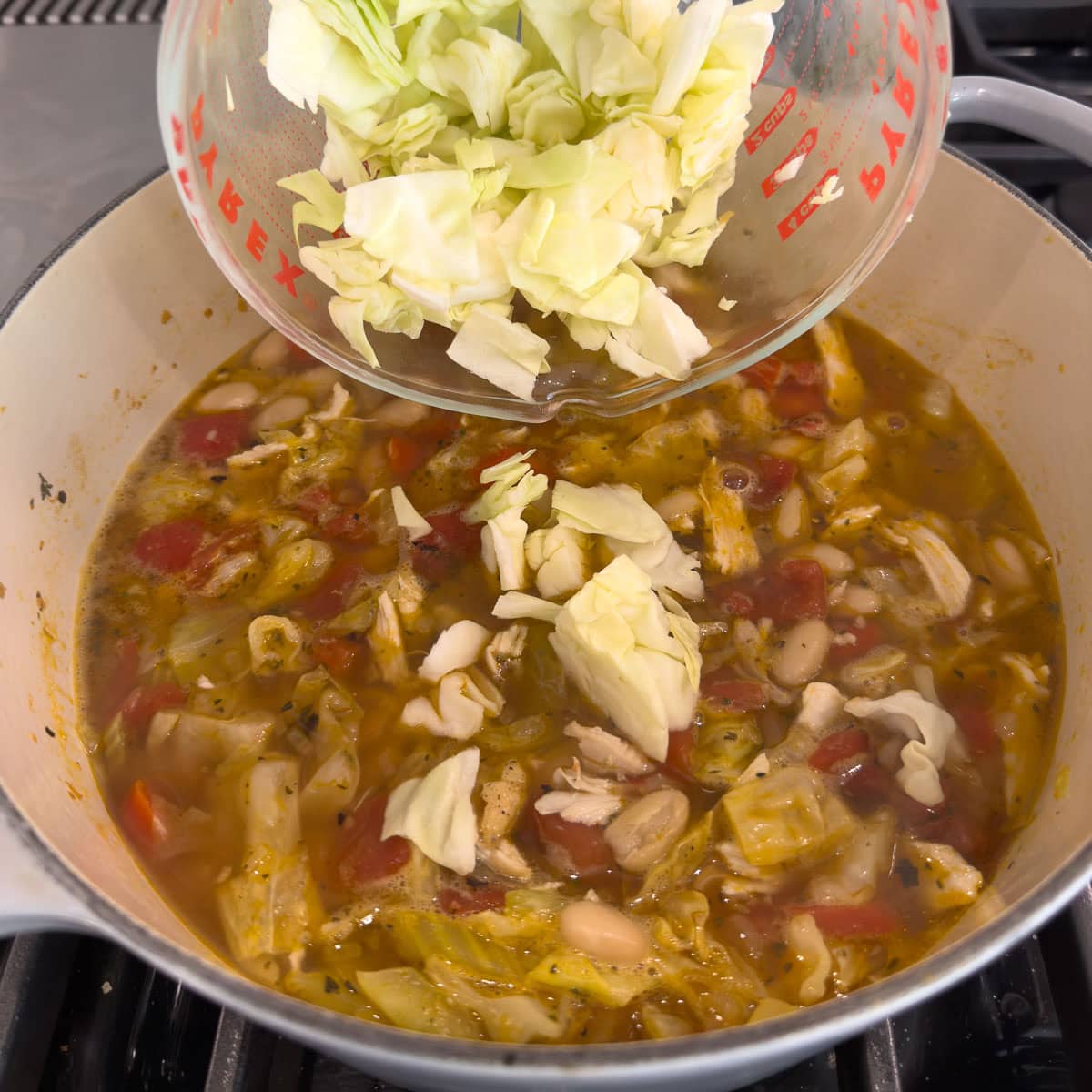 Adding cabbage to a pot of cabbage and chicken soup.